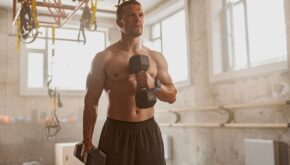 Man holding two dumbbells and raising one dumbbell to his chest using left arm during workout